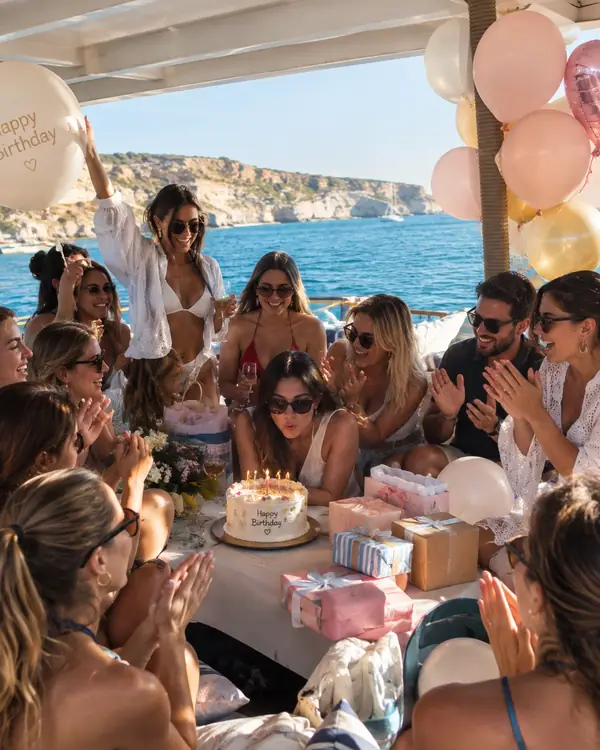 Friends clapping as the birthday girl blows out the candles on a cake aboard a private boat in Mallorca