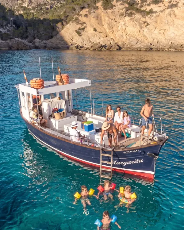 Family swimming in turquoise water next to the Margarita boat anchored in a cove in Mallorca